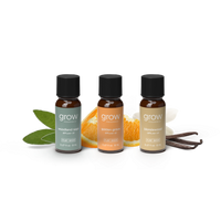 Three small amber glass essential oil bottles with black caps from grow naturally, arranged on a white background with flavor props including green leaves, orange slices, white blossoms, and vanilla beans. 