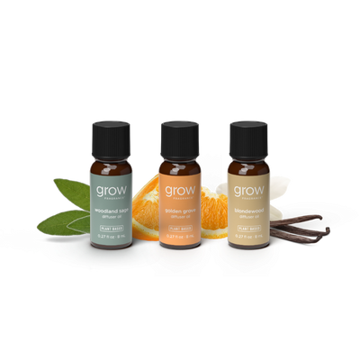 Three small amber glass essential oil bottles with black caps from grow naturally, arranged on a white background with flavor props including green leaves, orange slices, white blossoms, and vanilla beans. 