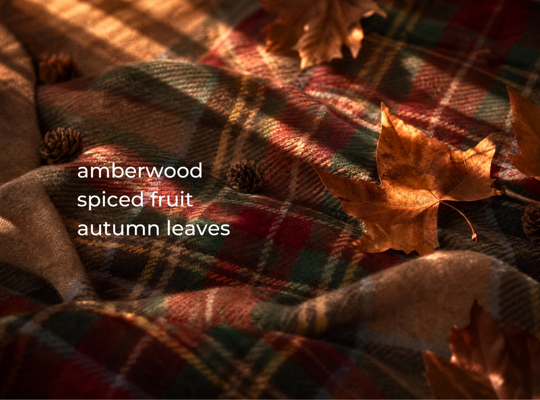 A close-up of a plaid fabric in autumn colors, draped with amberwood, spiced fruit, and fallen leaves. White text on the left reads 'amberwood spiced fruit autumn leaves'. (featured)
