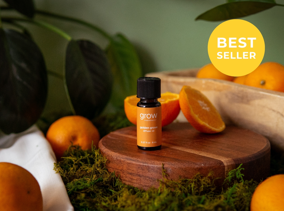 A small amber essential oil bottle labeled 'grow' stands on a round wooden pedestal surrounded by oranges, moss, and green leaves. A yellow circular badge in the top right reads 'BEST SELLER'. (featured)