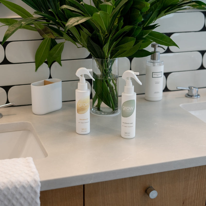 Grow Fragrance Non Toxic air and fabric sprays labeled 'Woodland Sage' and 'Blondewood' on bathroom countertop 