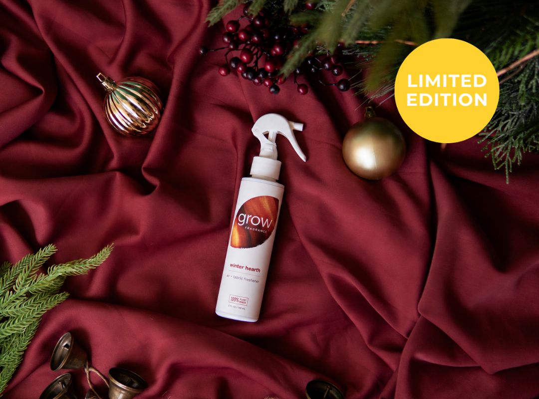 A white spray bottle labeled 'grow' lies on draped burgundy fabric with holiday decorations including pine branches, red berries, gold ornaments, and bells. A yellow circle in the top right says 'LIMITED EDITION'. (featured)