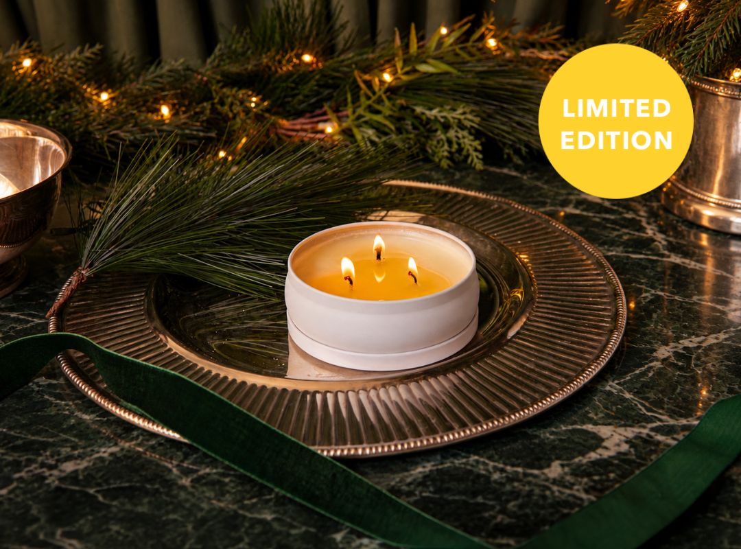 White candle in a tin surrounded by greenery and festive decorations on a dark surface (featured)