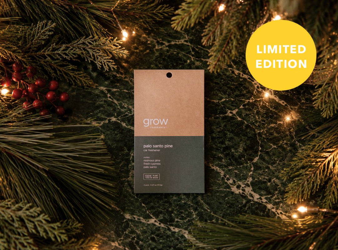A car freshener labeled 'grow' is centered on a dark green marble surface surrounded by pine branches, red berries, and warm string lights. A yellow circular badge in the top right reads 'LIMITED EDITION'. (featured)