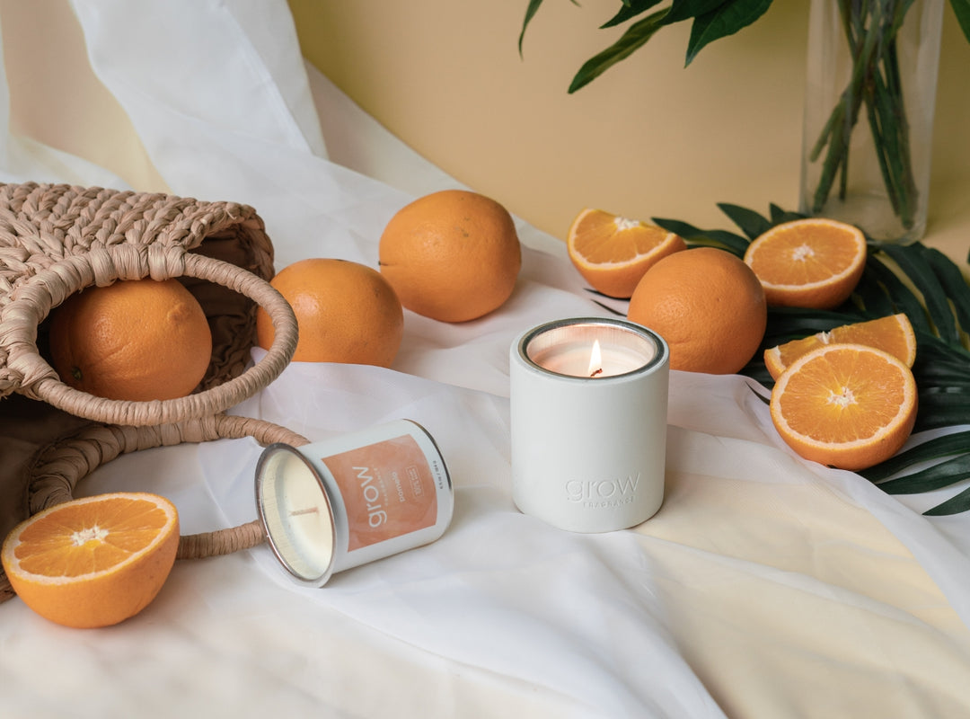 Pomelo Candle on orange backdrop surrounded by oranges and greenery (featured)