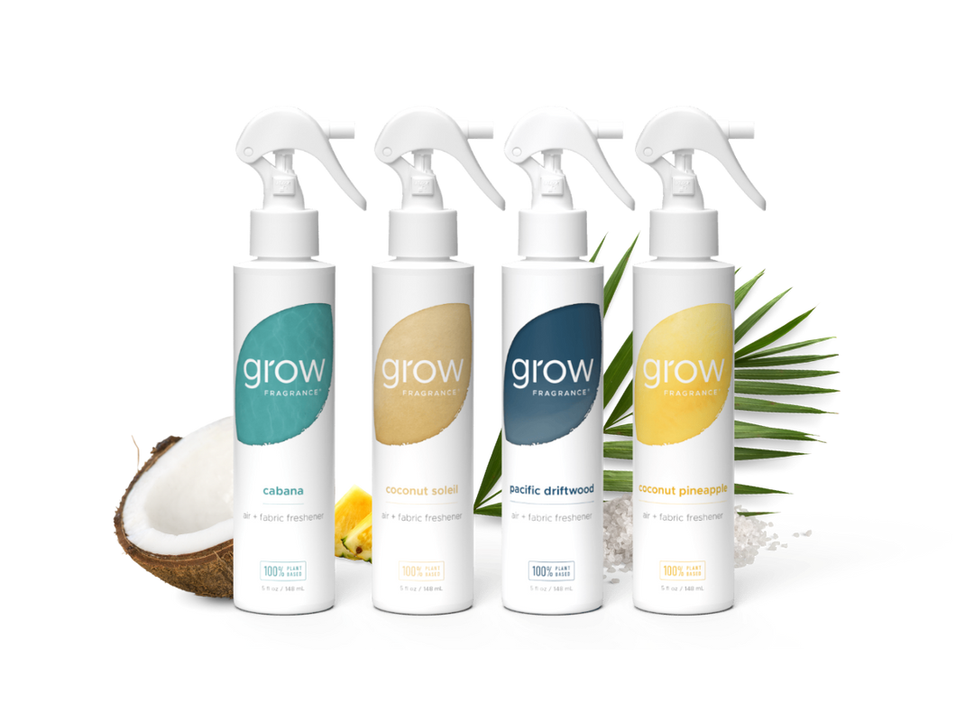 Four white spray bottles from the brand grow professionally lined up on a white background, styled with a halved coconut, lemons, and green palm leaves. The bottles feature colorful labels in teal, beige, navy, and yellow, representing the flavors: cabana, coconut sole, Pacific Delitt, and Coconut Pine森.