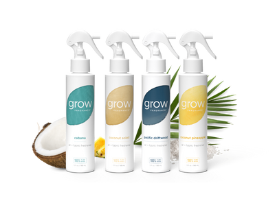 Four white spray bottles from the brand grow professionally lined up on a white background, styled with a halved coconut, lemons, and green palm leaves. The bottles feature colorful labels in teal, beige, navy, and yellow, representing the flavors: cabana, coconut sole, Pacific Delitt, and Coconut Pine森.