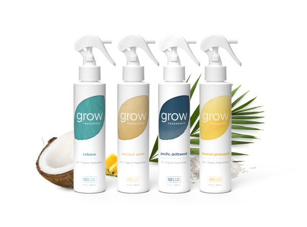 Four white spray bottles from the brand grow professionally lined up on a white background, styled with a halved coconut, lemons, and green palm leaves. The bottles feature colorful labels in teal, beige, navy, and yellow, representing the flavors: cabana, coconut sole, Pacific Delitt, and Coconut Pine森.