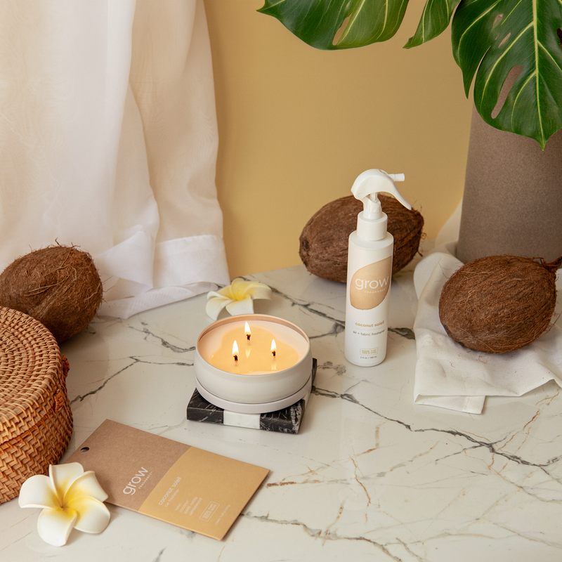 Candle, coconuts, and a bottle on a marble surface with a neutral background
