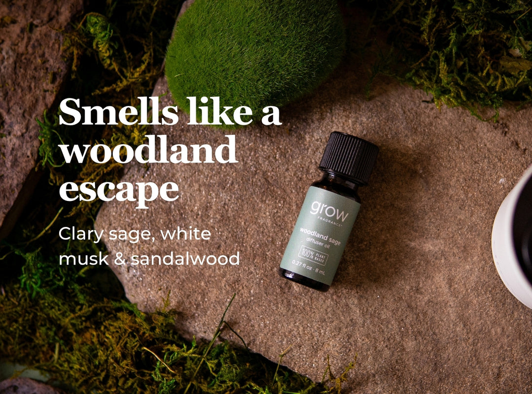 A small bottle of Grow Naturally essential oil labeled 'Clary sage, white musk & sandalwood' placed on a stone surface with moss around it. Large white text on the left reads 'Smells like a woodland escape'. (featured)