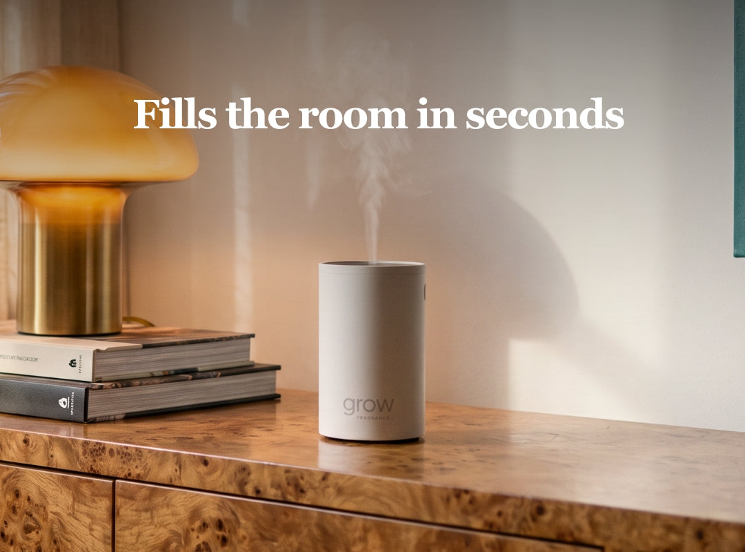 A cylindrical white grow diffuser emitting a visible plume of steam, placed on a wooden console table next to books and a gold lamp. White text at the top reads 'Fills the room in seconds'.
