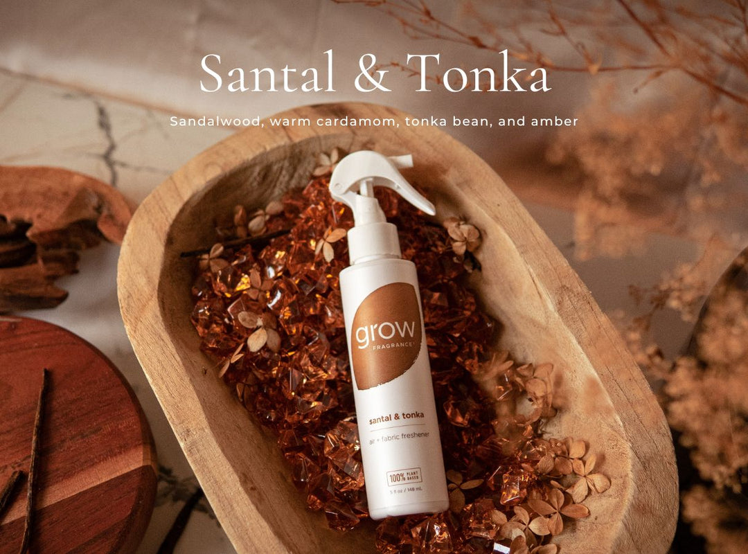 A white spray bottle labeled 'grow sanctuary Santal & Tonka' sits in a wooden bowl filled with warm brown botanical pieces, with dried floral elements and text reading 'Santal & Tonka' above. (featured)