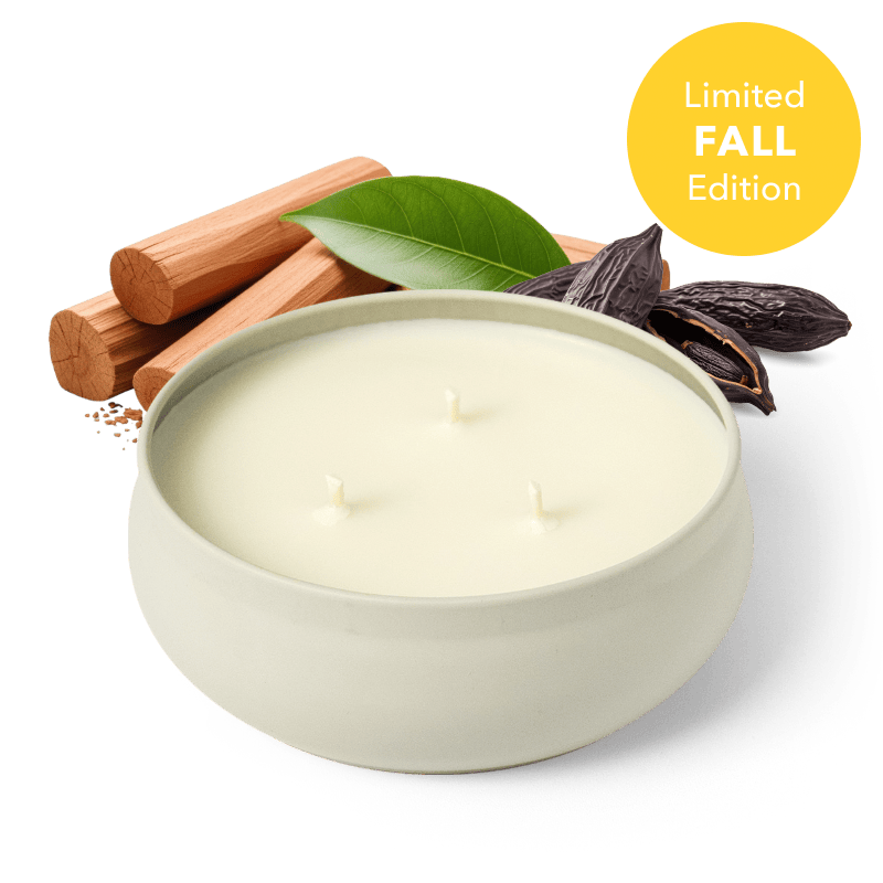 A white three-wick candle in a round white vessel, styled with cinnamon sticks, a green leaf, and dark cacao beans on a dark green background, with a yellow 'Limited FALL Edition' badge in the top right.