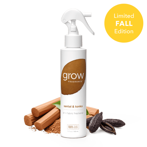 A white spray bottle of grow Fragrance santal & tonka air + fabric freshener centered on a dark green background, with cinnamon sticks, cocoa powder, and cacao beans arranged around the base. A yellow circle in the top right reads 'Limited FALL Edition'.