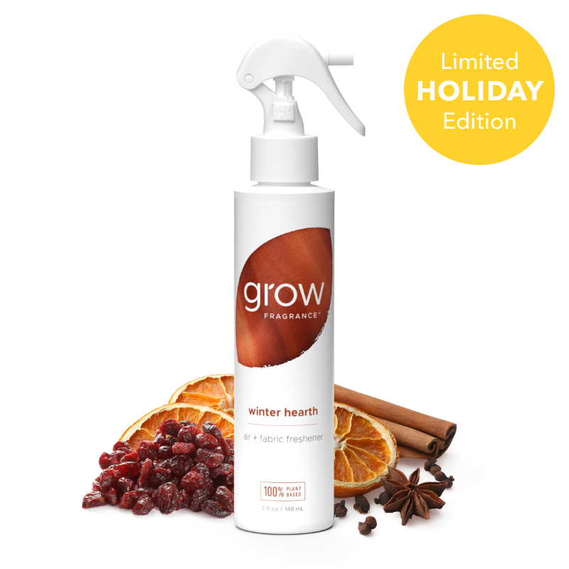 A white spray bottle of grow Fragrance 'winter hearth' air and fabric freshener, styled with dried orange slices, cranberries, cinnamon sticks, and star anise on a white background, with a yellow 'Limited Holiday Edition' badge in the top right.