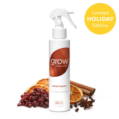 A white spray bottle of grow Fragrance 'winter hearth' air and fabric freshener, styled with dried orange slices, cranberries, cinnamon sticks, and star anise on a white background, with a yellow 'Limited Holiday Edition' badge in the top right.